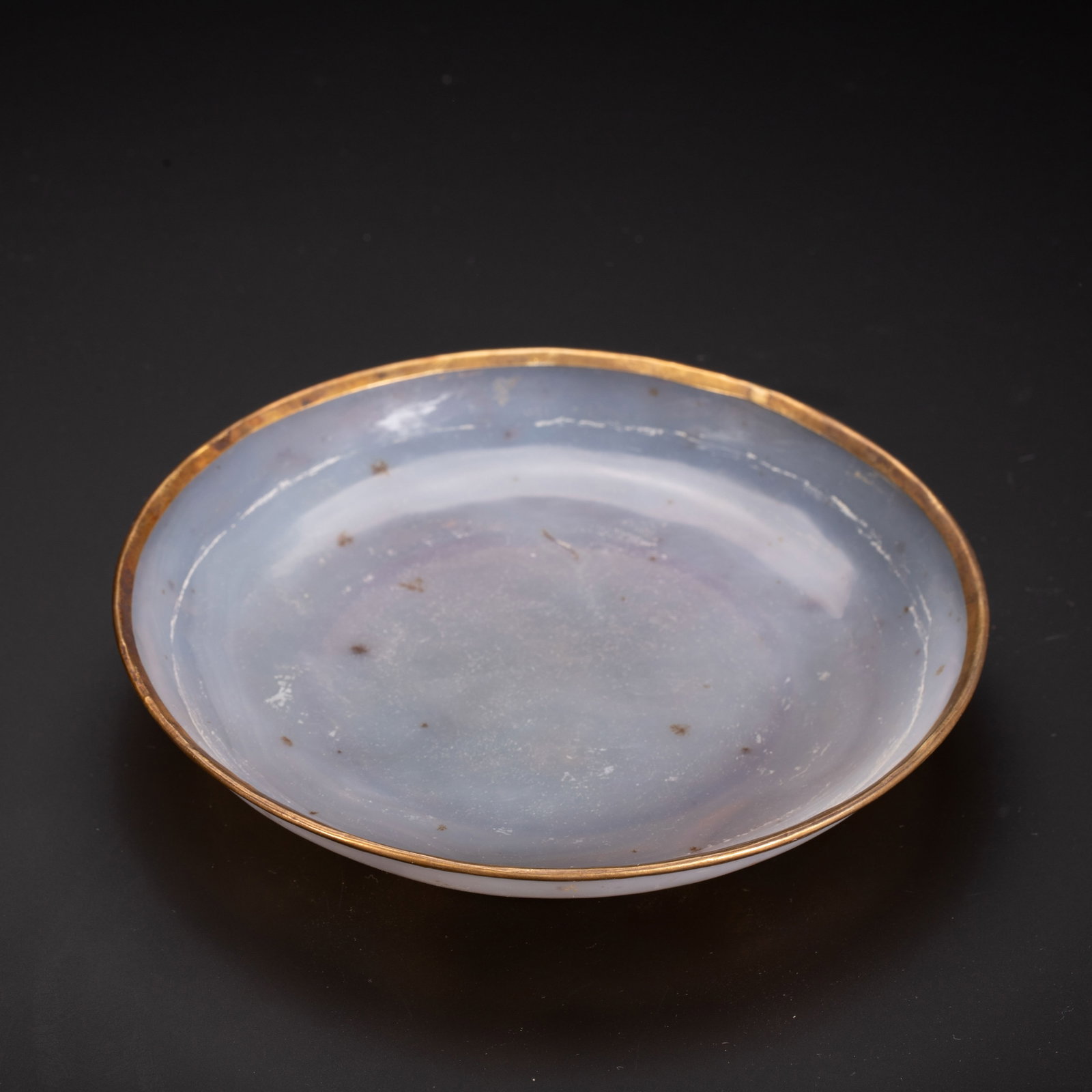 Chinese Gold-Rimmed Agate Dish: Chinese Gold-Rimmed Agate Dish A shallow circular dish carved from translucent pale agate, with a natural milky lavender hue and subtle dark speckles visible throughout the stone. The rim is neatly