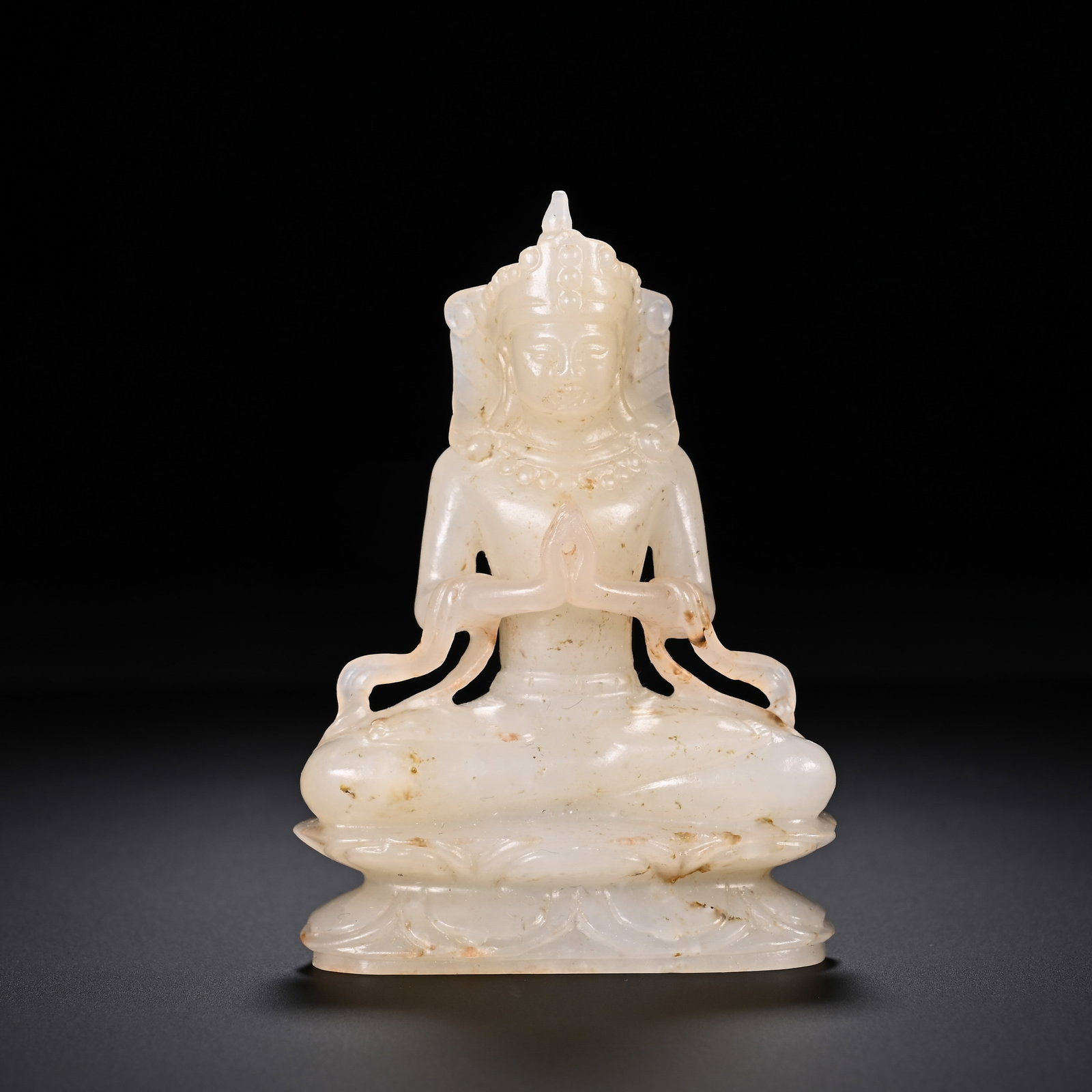 A Chinese Hetian Jade Buddha Figure: A Chinese Hetian Jade Buddha Figure A serene Chinese Hetian jade Buddha figure, carved in lotus position with hands pressed together in prayer. The figure wears an ornate crown and beaded adornments, 