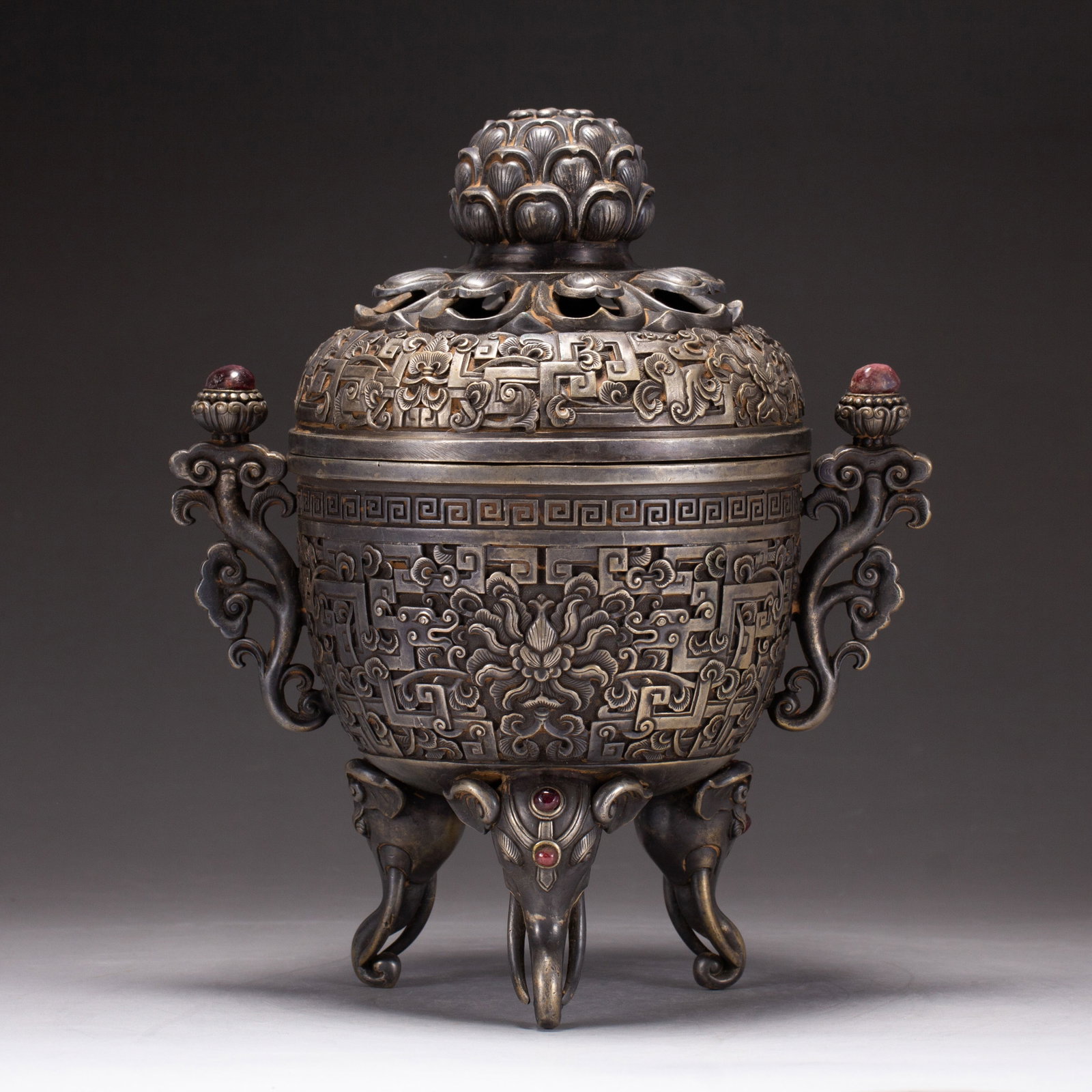 Chinese Silver-Inlaid Bronze Tripod Censer: Chinese Silver-Inlaid Bronze Tripod Censer An ornate tripod censer cast in bronze with a rich patina, featuring elaborate silver-inlaid and relief-carved decoration. The body displays central floral m