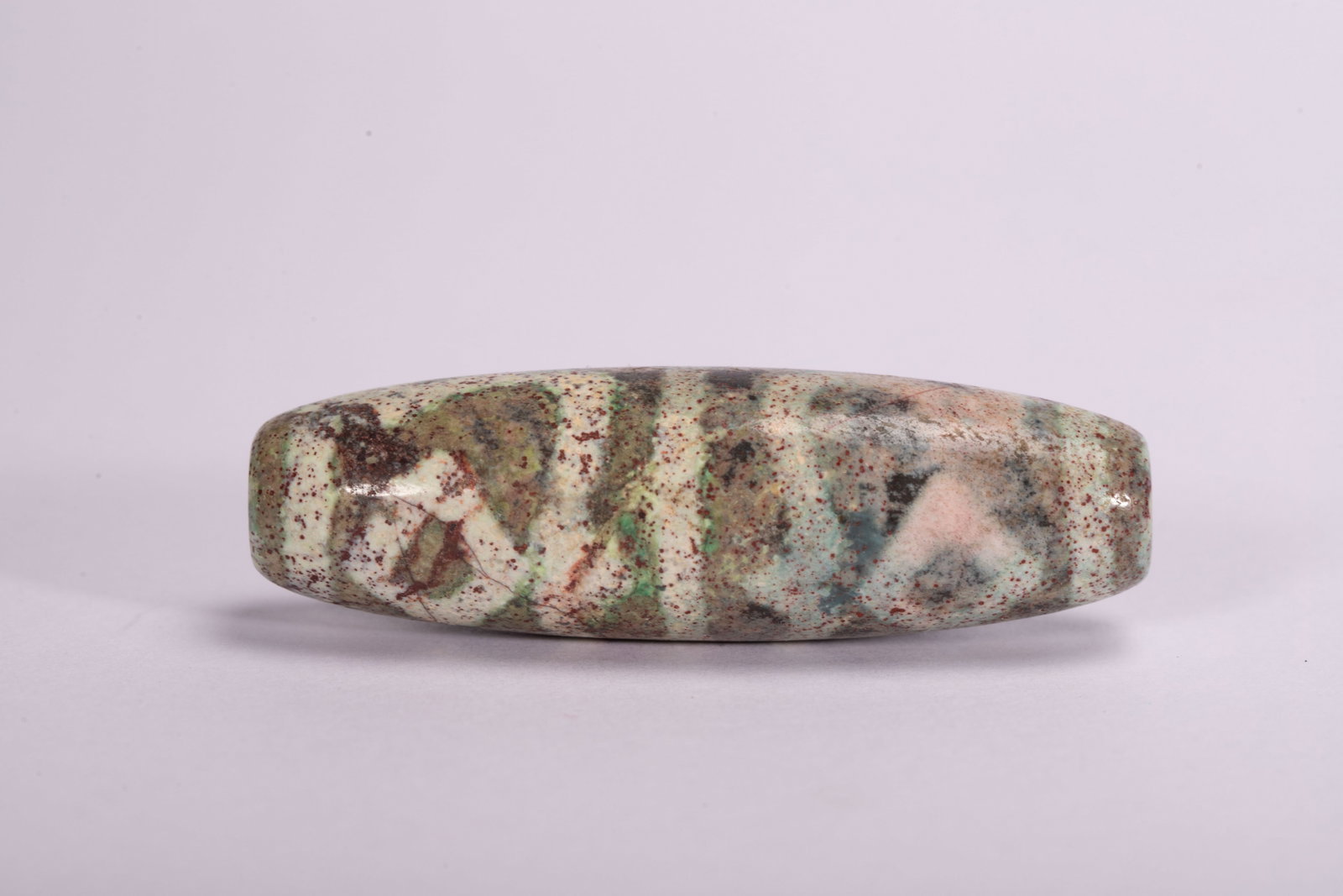 Chinese Dzi Bead with Natural Patterns: Chinese Dzi Bead with Natural Patterns This striking dzi bead measures 6 cm in length and weighs 30 grams. The cylindrical stone bead displays a natural, mottled pattern of white, green, and earthy to