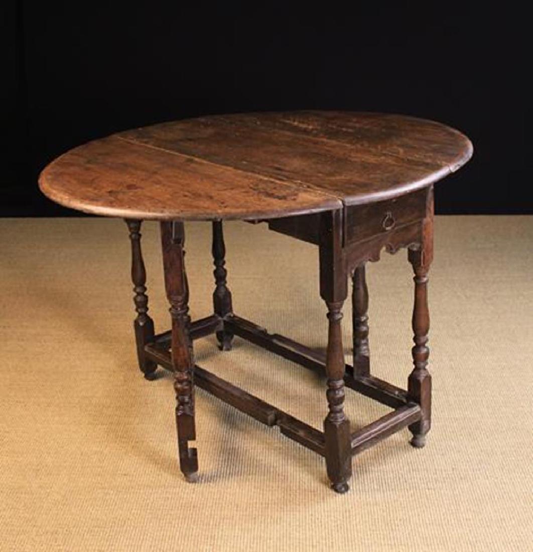 An 18th Century Oak Gateleg Table (A/F). The oval top: An 18th Century Oak Gateleg Table (A/F). The oval top standing on urn-knopped baluster legs & gates united by moulded stretchers and terminating on turned feet. One end fitted with a drawer. 28½in (7