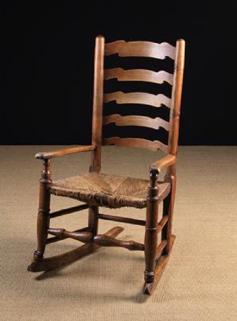An Early 19th Century Lancashire Ladder-backed: An Early 19th Century Lancashire Ladder-backed Rush-seat Rocking Chair. The five wavy-cut graduated back 'rungs' between round turned uprights. The swept arms on urn knopped posts leading on to form t