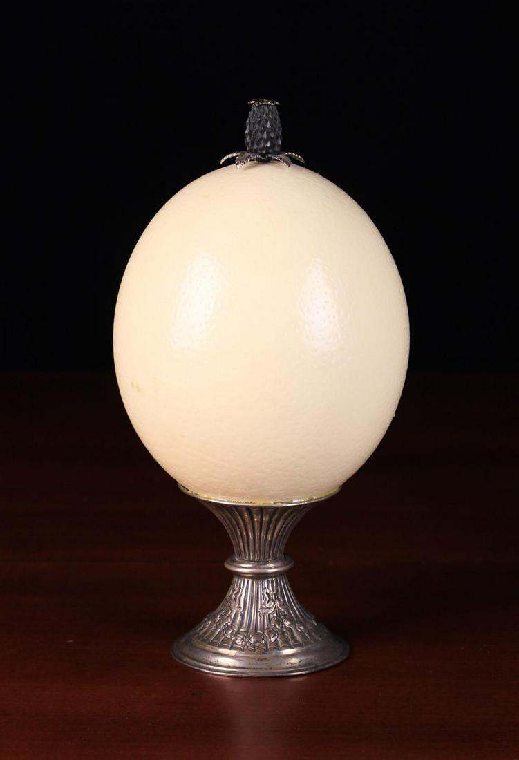 A Silver Mounted Ostrich Egg. The Victorian silver: A Silver Mounted Ostrich Egg. The Victorian silver pedestal hallmarked Birmingham 1887 and stamped with George Unite's maker's punch. The egg surmounted by a carved ebony & silver pineapple finial, 9�