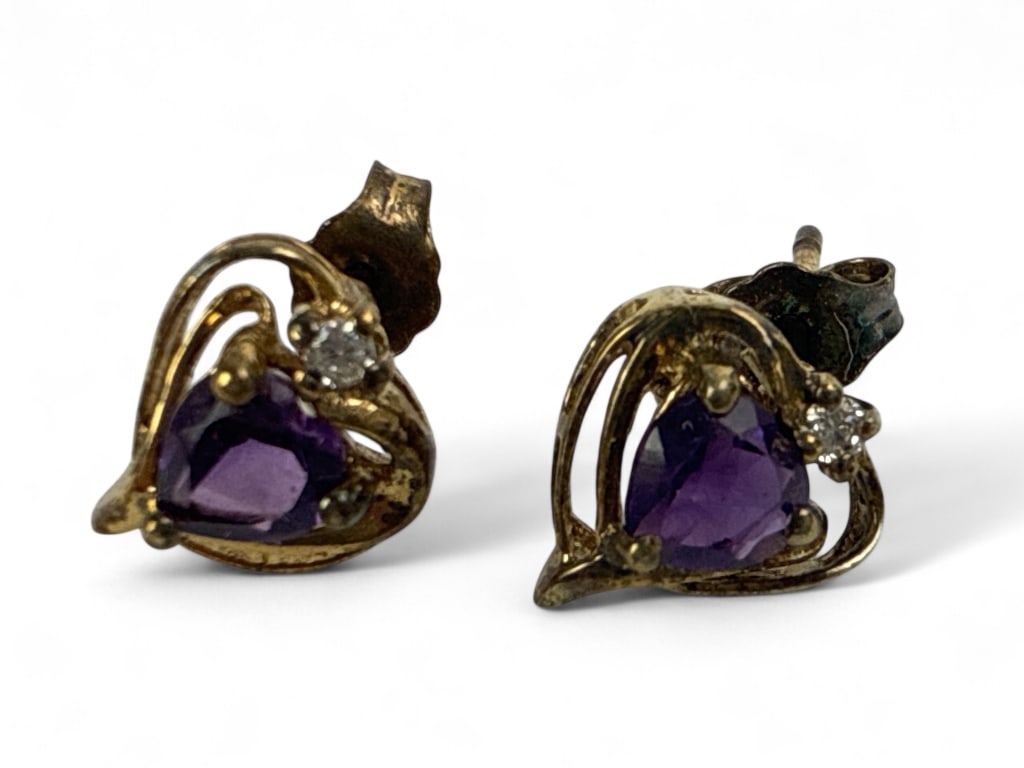 Sterling And Amethyst Heart Earrings: Sterling silver stud earrings featuring heart-shaped amethyst stones set within an open heart design. Marked 925, indicating sterling silver purity. Includes accompanying small clear accent stones. Co