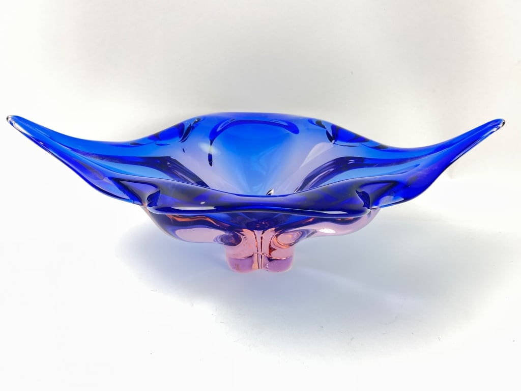 Blue and Pink Murano? Glass Bowl: Murano style glass bowl featuring a combination of vibrant blue and pink hues. Designed in a stretched, wing-like form, the bowl includes a four-sided base. Dimensions are 16 3/4" by 9.5" . The base h