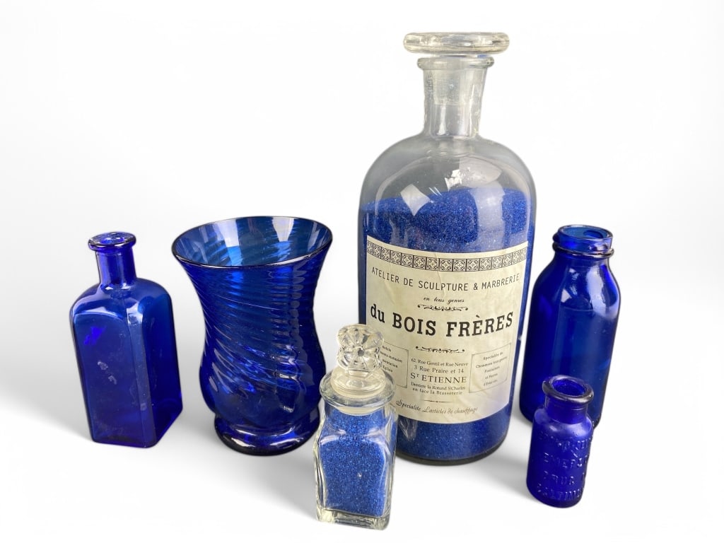 Collection Of Blue Glass Bottles And Jar: Collection includes six cobalt blue glass bottles and one glass jar with label reading 'du Bois Freres'. Includes varying embossed details. The large jar and one smaller bottle contain blue granules.