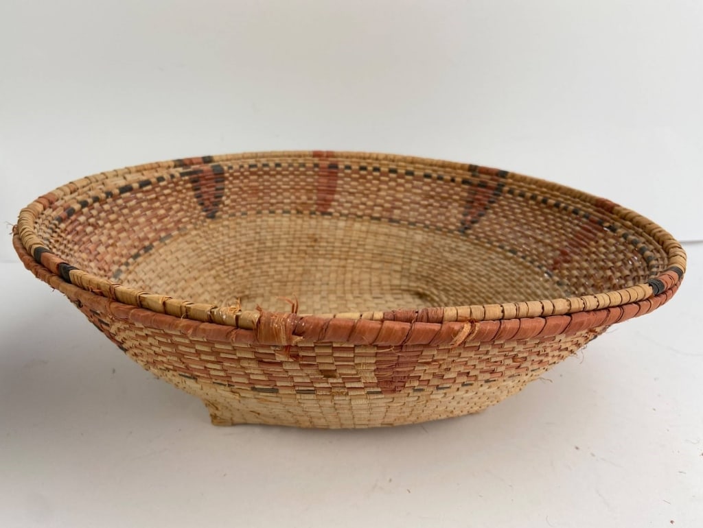 Native American Handwoven Basket: Handwoven Possibly Native American basket with intricate designs featuring natural and dyed fibers. The basket displays a blend of beige, red, and black patterns. Notable for its craftsmanship.