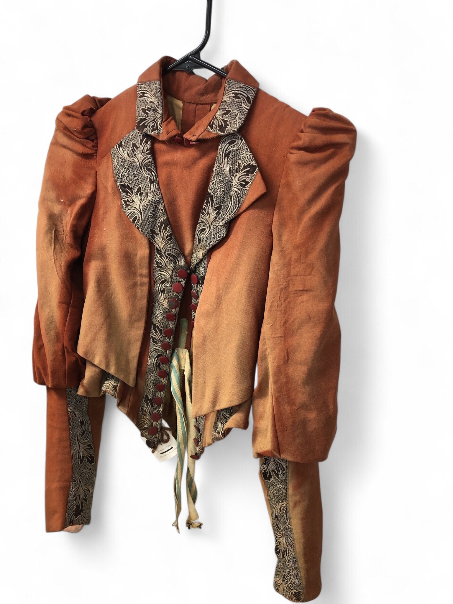 Brown And Black Tailored Waistcoat: Turn-of-the-century brown and black waistcoat featuring detailed tailoring and decorative accents, including embroidered black leaf-like patterns, red fabric buttons, and ribbon ties. Noticeable wear 