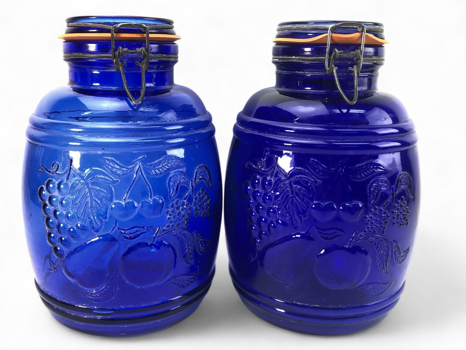 Two Casidis Milano Cobalt Canisters: Vintage Casidis Milano cobalt blue barrel canisters with embossed fruit design and bail stopper bottle closures. Each measures 10.5 inches tall with lids shut. Minor chip noted.