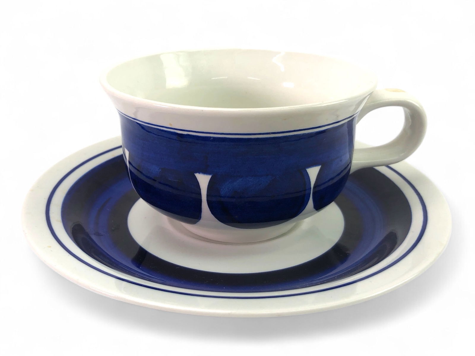 A Rörstrand ‘Colette’ Cup and Saucer, designed by Inger Persson: Inger Persson for Rorstrand Sweden “Colette” cup and saucer. Features hand-painted blue-on-white design. Saucer diameter is 7 inches, and the cup is 2.5 inches tall. Some wear present, includi
