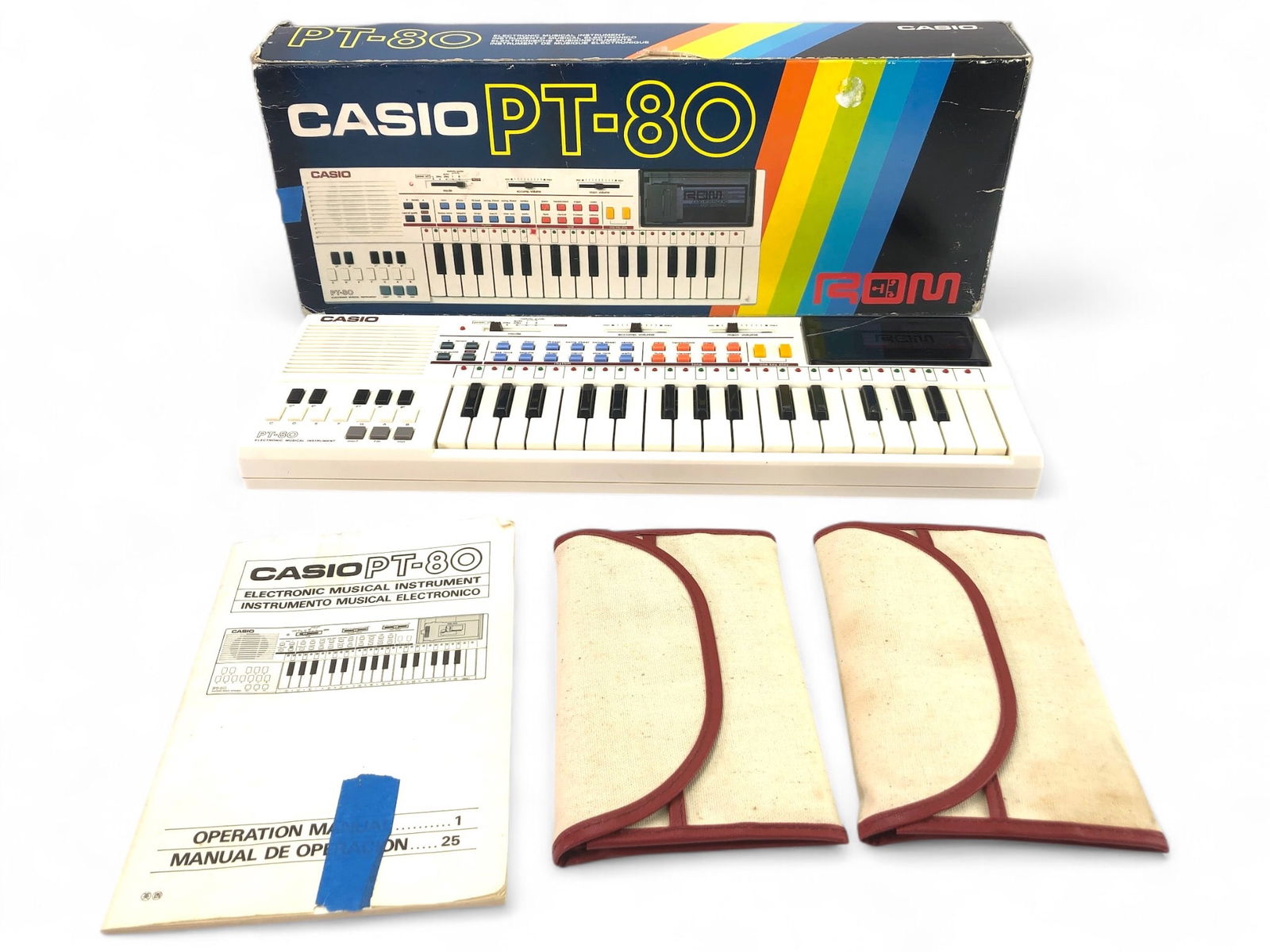 1980s Casio PT-80 Keyboard With Accessories: Casio PT-80 electronic keyboard from the 1980s, includes 5 ROM packs, 2 storage cases, and the original operation manual. Battery compartment exhibits some corrosion. Includes the original box with vi