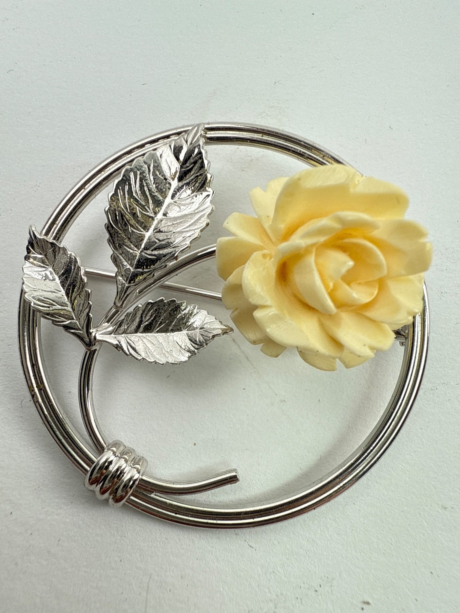 Mid-Century Sterling Brooch W Carved Rose: Mid-century sterling silver brooch featuring a carved cream-colored rose, accented by detailed silver leaf designs. The brooch is signed "Sterling" on the back with makers mark. It measures 1.5 inches