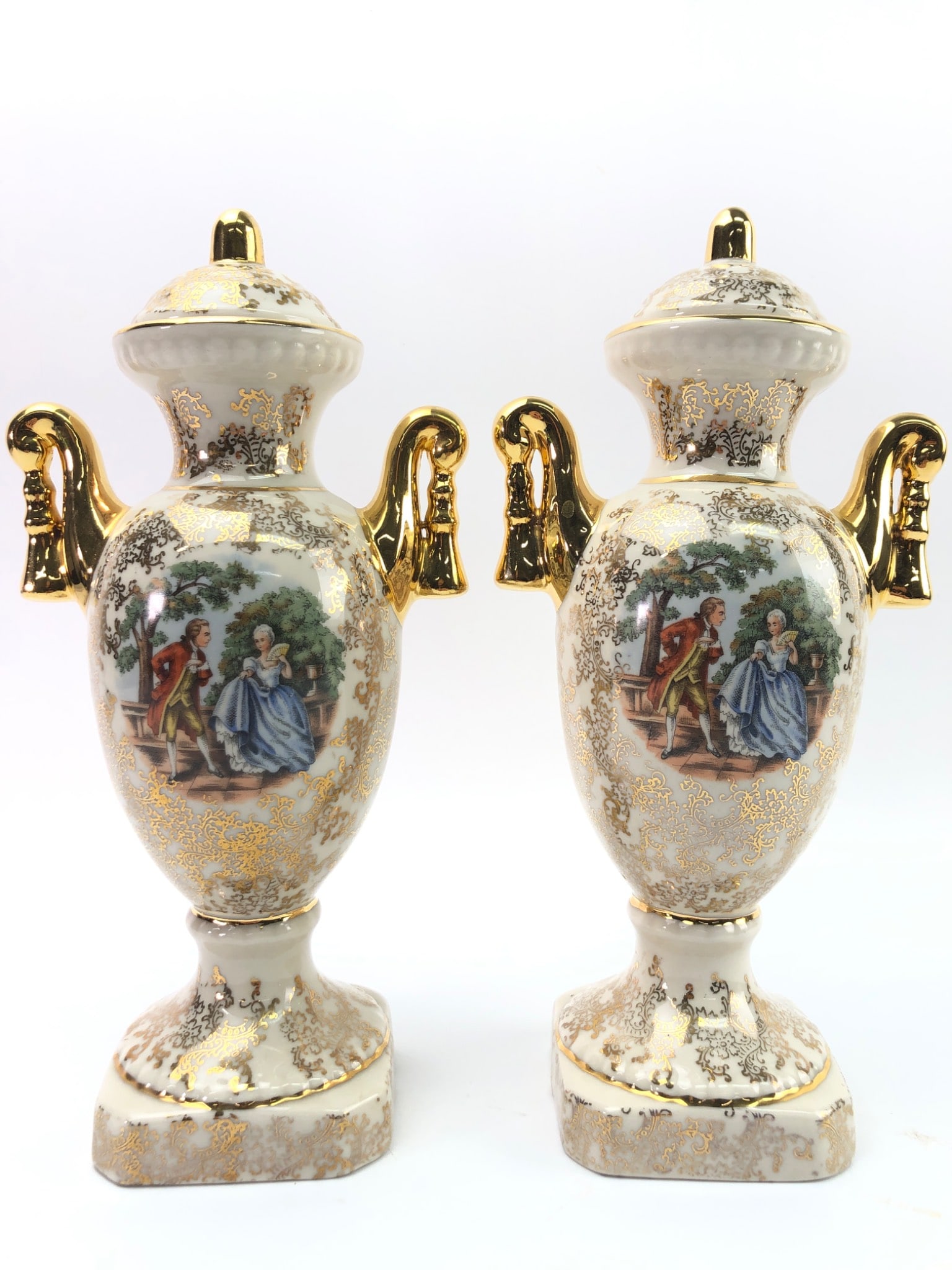 Rococo Revival Gilt Porcelain Urns: Rococo Revival style gilt porcelain covered urns, marked 'U.S.A.' and 'Hand Decorated Warranted 22 K. Gold.' Featuring detailed painted scenes and gold accents. Each measures approximately 10 inches t