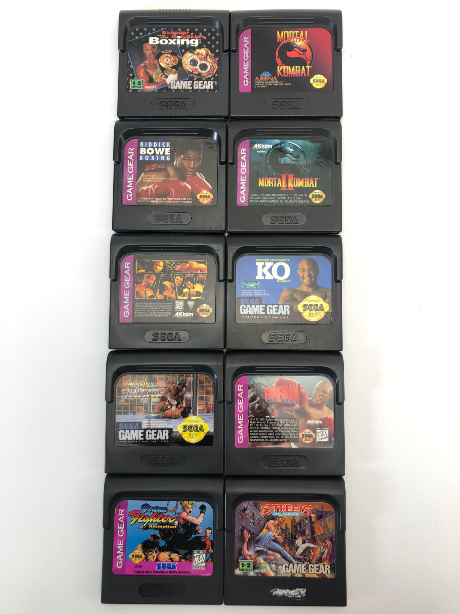 10 Sega Game Gear Fighting Games: 10 Sega Game Gear fighting games, including titles such as Mortal Kombat, George Foreman's KO Boxing, Streets of Rage, and more. Cartridges exhibit signs of use, with visible wear on some contact edge