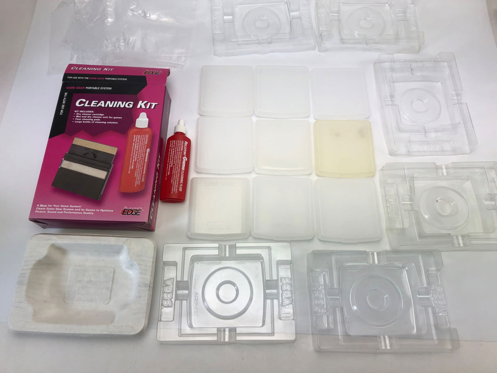 Game Gear Plastic Cases & Cleaning Kit: Several plastic cases for Sega Game Gear cartridges, one cleaning kit by Player's Edge with a cleaner unit, fluid bottle, and pads, plus plastic slip bags for games. Wear and discoloration on some cas
