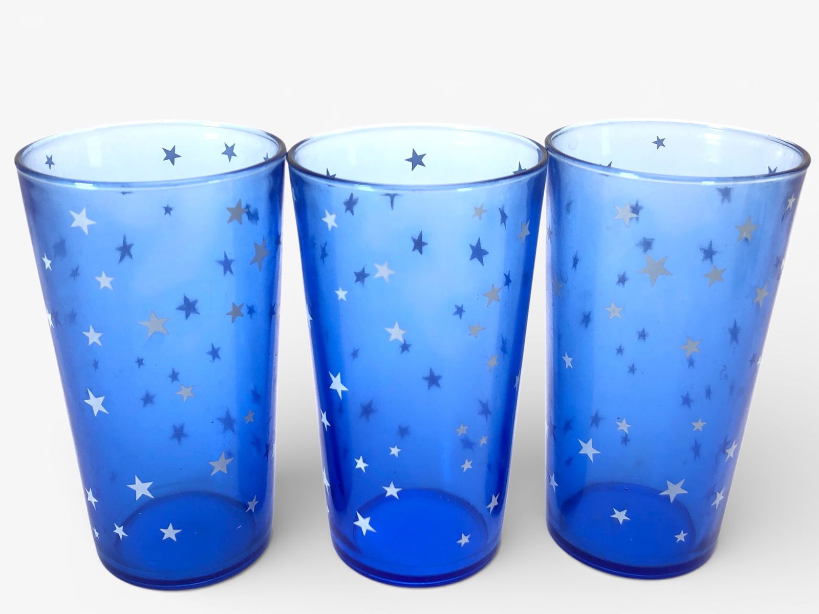 Rare Hazel-Atlas Star Ritz Cobalt Tumblers: Three Hazel-Atlas Star Ritz cobalt blue tumblers featuring a silver star pattern. Each tumbler stands approximately 5 inches tall. Made of glass, the tumblers showcase a vibrant cobalt hue. A classic