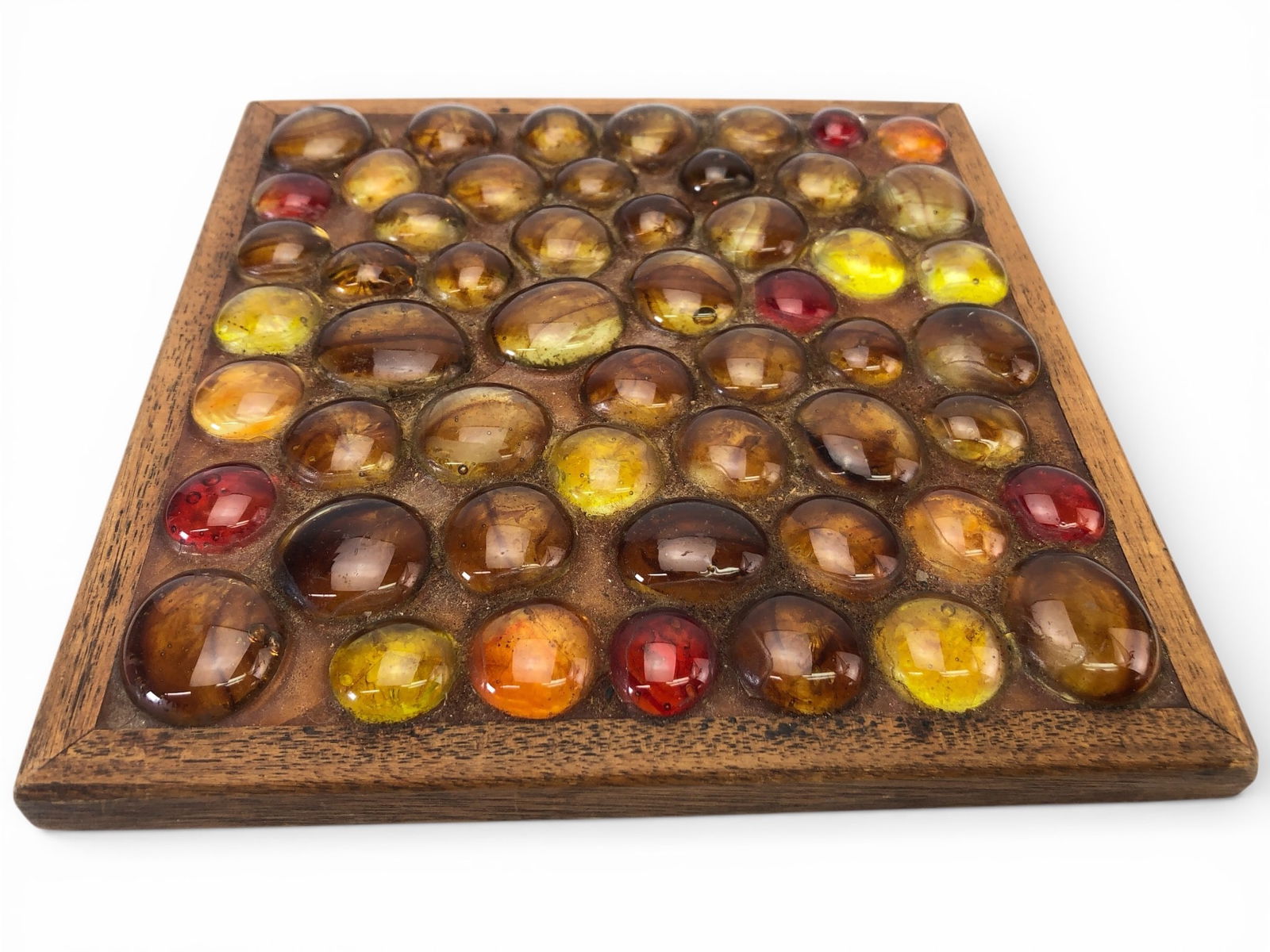 Vtg Pebble Glass In Wood Frame Trivet: Vintage trivet featuring multicolored pebble glass set in a square wooden frame. Measuring 6 3/4 x 6 3/4 inches, this piece is designed for decorative or functional use. Bottom includes red glass