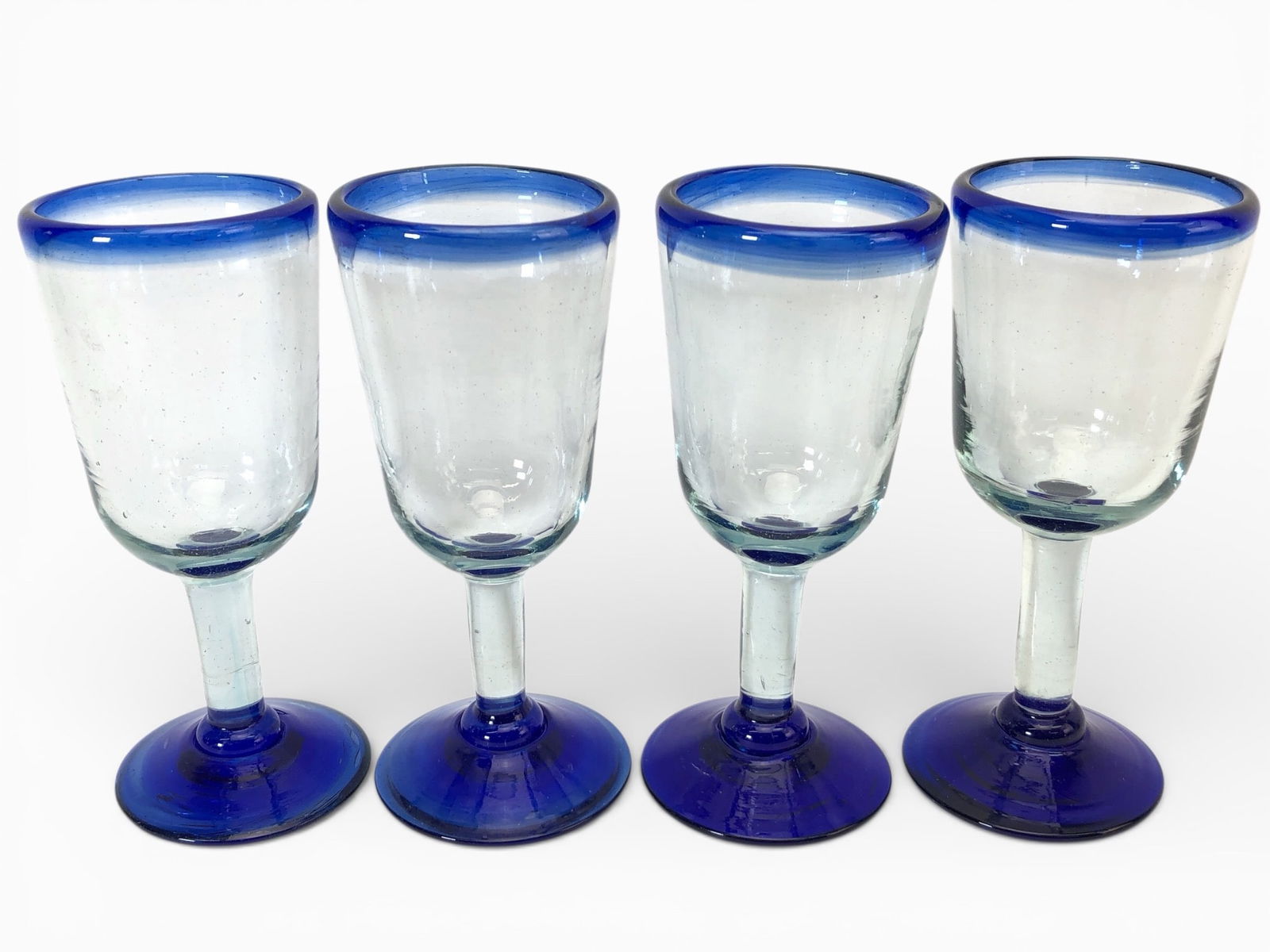 4 Hand Blown Cobalt Blue Rim & Stem Goblets: 4 hand-blown goblet glasses with cobalt blue stems & rims. Approx. 6.5 inches tall. Clear glass with visible handcrafted details, showcasing a unique design. Perfect addition to glassware collections