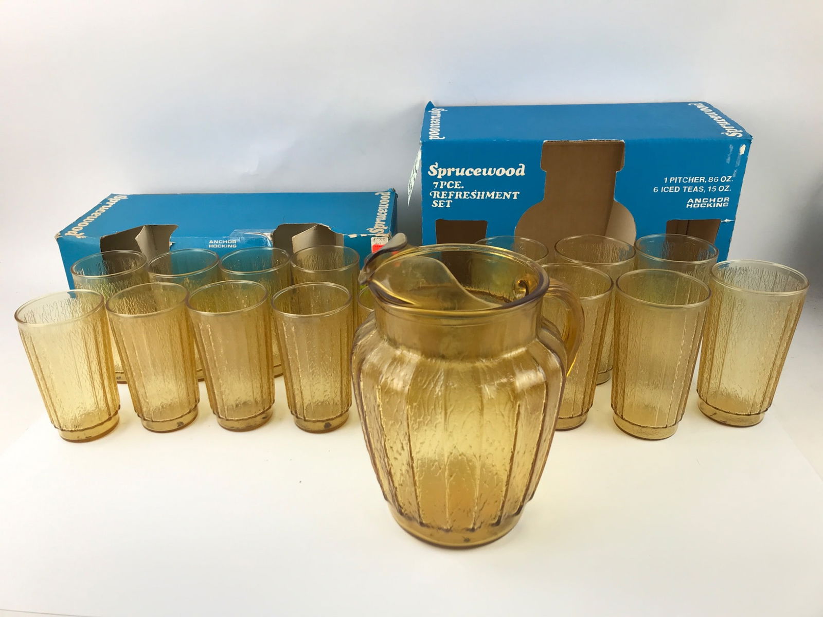 Original Boxes 1970’s Anchor Hocking Sprucewood Glassware Set: Anchor Hocking Sprucewood glassware set featuring amber-colored textured glass. Includes an 85 oz pitcher (10” tall, 3” diameter) with a spout & handle, 6 iced tea glasses (15 oz, 6”