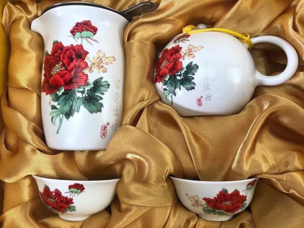 Chinese Tea Set In Gift Box: Chinese tea set in a gift box including one teapot with a yellow-braided lid retainer, one pitcher with a metal strainer, and two tea cups. Each porcelain piece features floral designs with red peonie