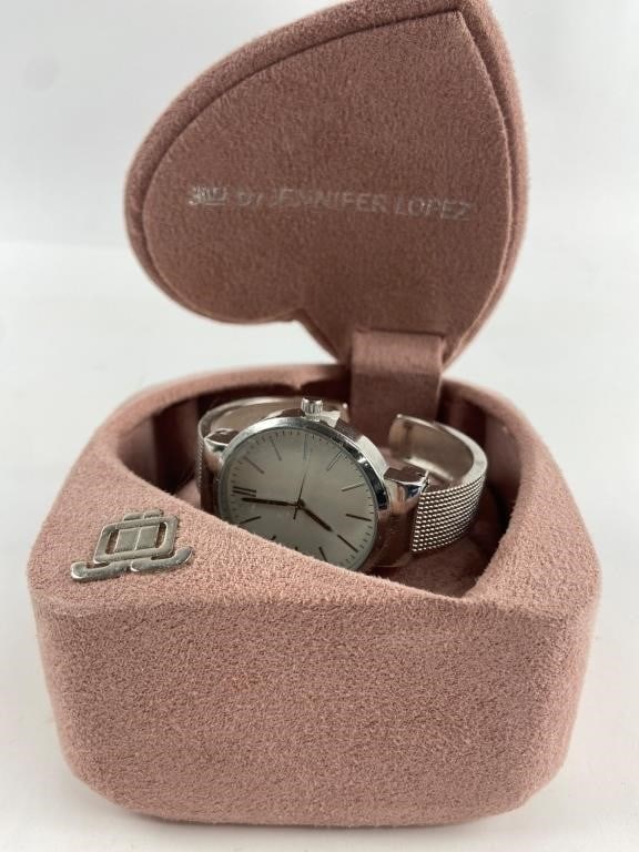 JLO Jennifer Lopez Watch In Heart Case: Silver-tone JLO Jennifer Lopez watch with a sleek round face, minimalist hour markers, & a mesh band. Housed in a dusty pink, heart-shaped case with a small metal emblem. Includes original branded