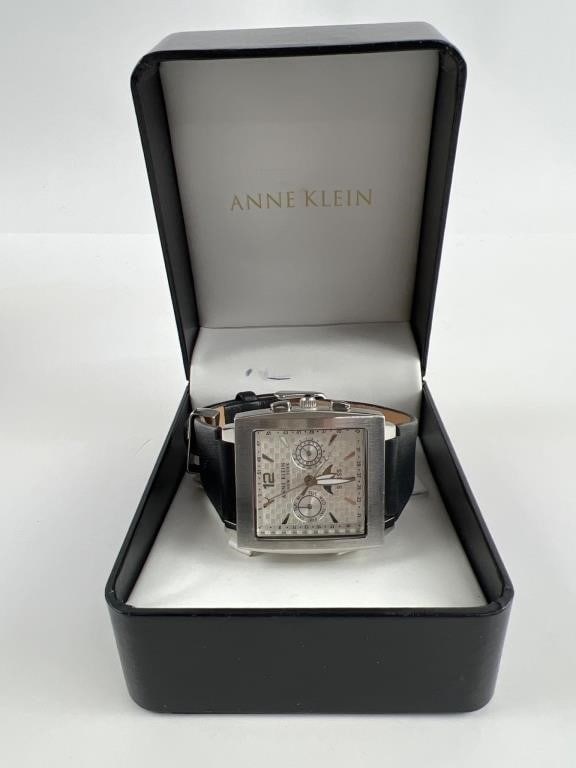 Anne Klein Swiss Men"s Leather Watch: Anne Klein Swiss men"s watch featuring a rectangular silver-tone case with a textured dial. Includes day, date, & moon phase displays. Black leather strap with a traditional buckle closure. Comes in o