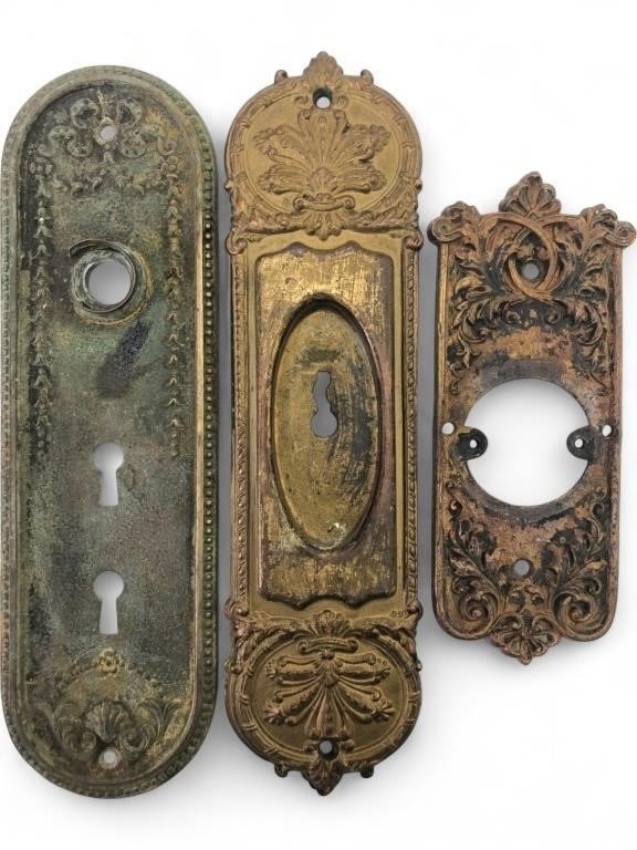 Assorted Victorian Style Brass Door Escutcheons: A group of three assorted Victorian style door escutcheons. Includes one long oval-top plate with beaded border and double keyholes, one ornate Neoclassical style plate with acanthus leaf and shell mo