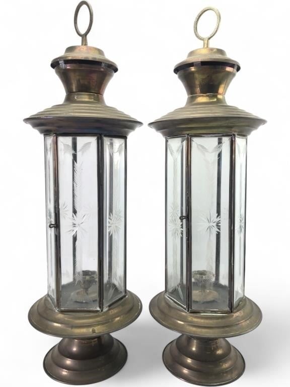 Pr. Etched Glass and Brass Hurricane Lanterns: A pair of tall hurricane-style lanterns featuring brass frames and etched glass panels. Each lantern has a hexagonal body with glass panels decorated with starburst and wheat motifs. The brass compone