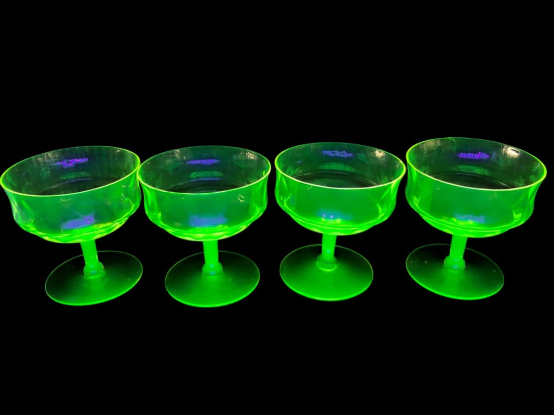 VTG Uranium Glass Optic Rib Champagne Coupes: Set of four uranium glass champagne coupe glasses featuring an optic rib pattern. The glasses exhibit a strong green fluorescence under UV light. Unmarked. One glass shows chips to the rim. 3 3/4" tal