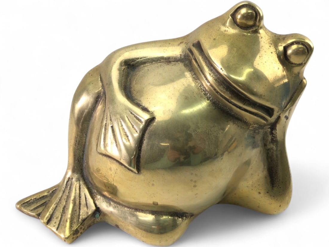 VTG Brass Reclining Frog Figure: Vintage polished brass figurine depicting a whimsical reclining frog. The figure features a smooth, rounded body with stylized webbed feet and prominent eyes. Unmarked. Shows scattered surface wear,