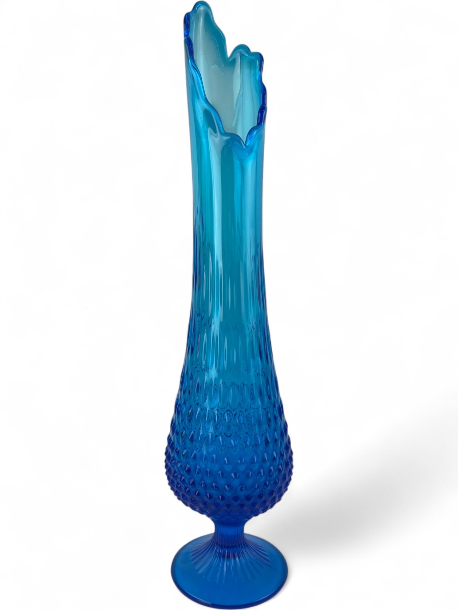Fenton Blue Hobnail Swung Glass Vase, 19.5": A tall swung glass vase by Fenton Art Glass. Crafted in a vibrant blue glass, it features a hobnail pattern on the lower body, a slender neck, and a ruffled, flame-like rim. The piece sits on a