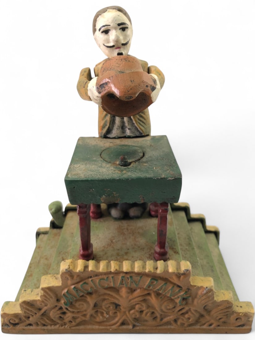 Antique Cast Iron Magician Mechanical Bank: Antique cast iron mechanical coin bank, 7.5" tall. Unmarked, attributed to late 19th/early 20th C. American manufacturers. Depicts a magician holding a hat over a table, with 'MAGICIAN BANK' embossed 