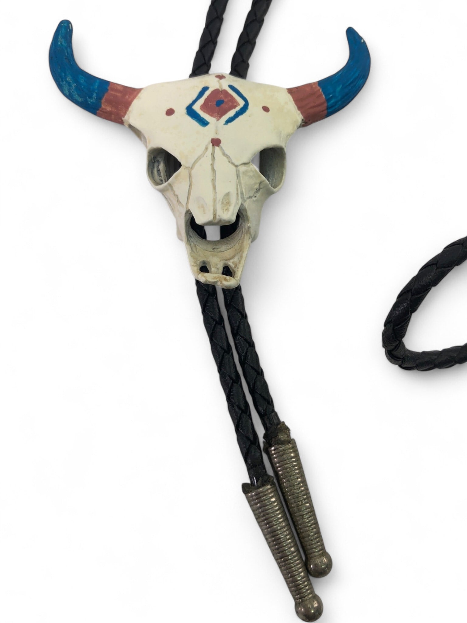 Hand-Painted Ceramic Bull Skull Bolo Tie: Hand-painted ceramic bolo tie featuring a stylized bull skull motif with blue and red accents. The skull is mounted on a black braided cord with ribbed silver-tone metal tips. Shows some wear to the p