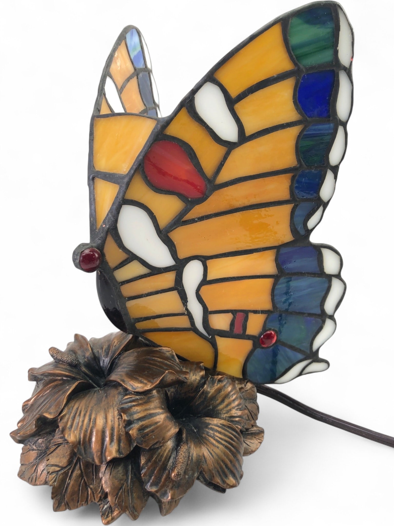 Tiffany Style Stained Glass Butterfly Accent Lamp: Tiffany style stained glass butterfly accent lamp featuring a multi-colored slag glass shade with red, blue, green, and amber tones. The piece is mounted on a cast metal base detailed with a floral hi