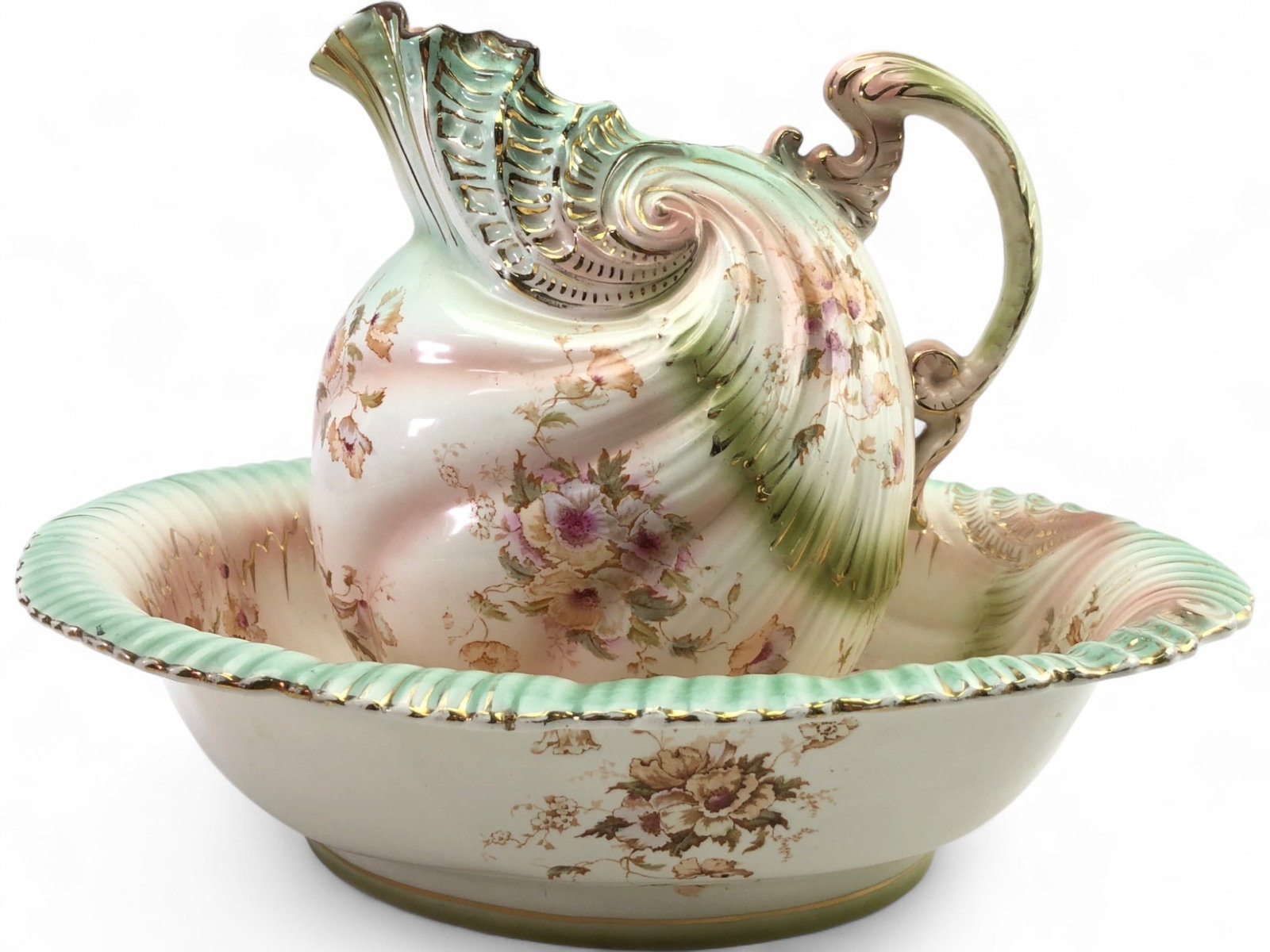 Victorian Style Floral Porcelain Pitcher and Basin: A Victorian style porcelain pitcher and wash basin set featuring a shell-molded design with hand-painted floral motifs and gilt accents. The set is decorated with pink and green ombre shading. The