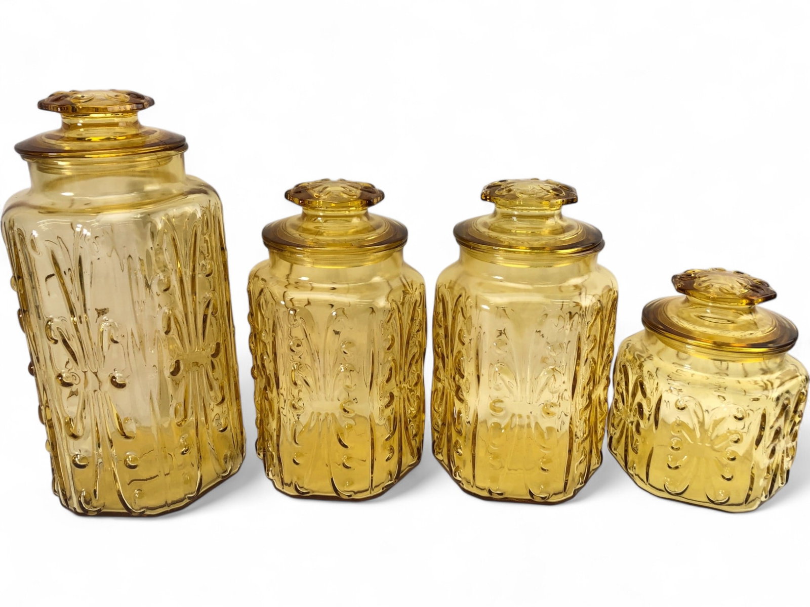 MCM LE Smith Atterbury Scroll Glass Canister Set: Set of four Mid-Century Modern amber pressed glass canisters in the Atterbury Scroll pattern by L.E. Smith. Features textured scroll and dot motifs with matching lids. Includes four sizes: tallest is 