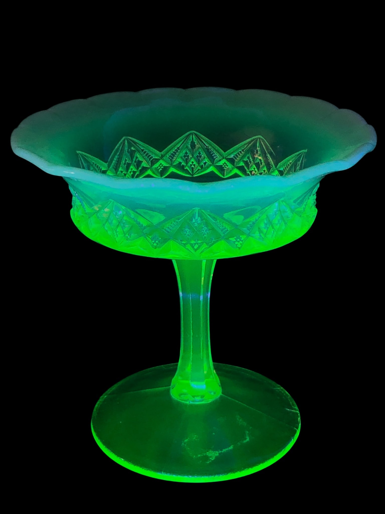 Northwood Spearhead Vaseline Opalescent Candy Dish: Pedestal candy dish attributed to Northwood in the Spearhead pattern. Crafted from vaseline opalescent pressed glass with a scalloped rim. Features a geometric diamond motif and glows bright green und