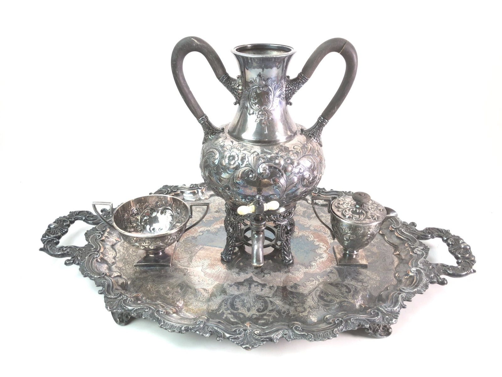 Victorian Style Silverplate Samovar and Tray Set: A Victorian style silverplate tea service featuring a large samovar with repoussé floral motifs, twin wooden handles, and an ivory-colored tap handle. Set includes a matching waste bowl, lidded