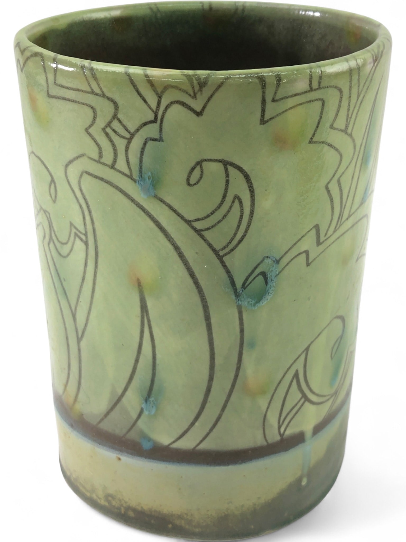 Signed Studio Art Pottery Vase: Studio art pottery vase, featuring a light green glaze with incised stylized floral and leaf patterns. Accented with blue drips and colorful speckles. The base has a darker band, and the interior is d