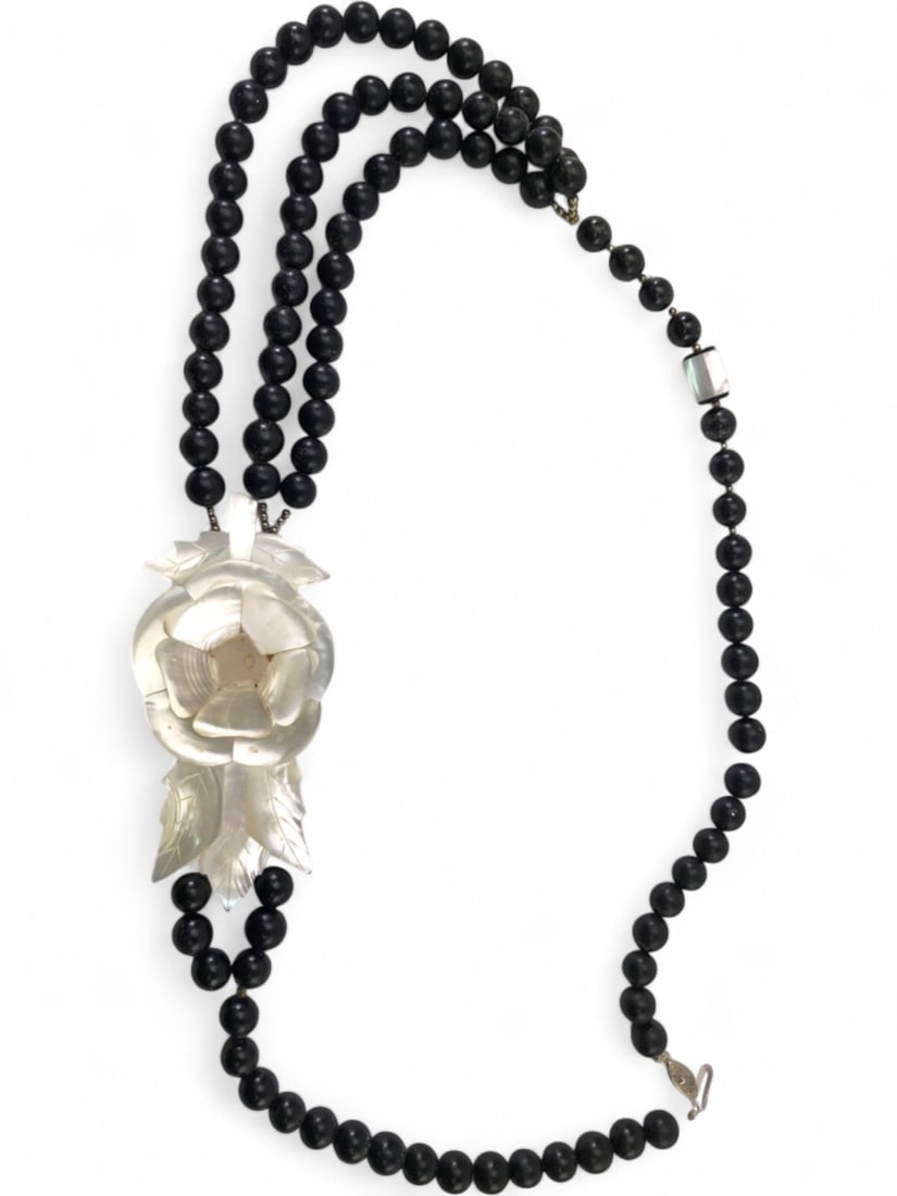 Mother-of-Pearl & Black Bead Floral Necklace: Vintage necklace featuring a large carved mother-of-pearl floral pendant with layered petals and leaves, backed by dark resin. Strung with black beads, likely wood, and a rectangular mother-of-pearl a