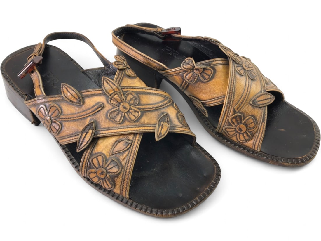 VTG Prada Embossed Leather Floral Slingback Sandals: Pair of Prada slingback sandals crafted from tan and dark brown genuine leather. Features an embossed floral and leaf pattern on criss-cross straps, a low block heel, and buckle closure. Marked "PRADA