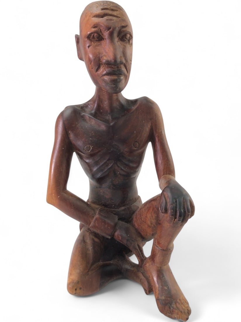 Signed Hand Carved Wood Seated Figure, 10" tall: Hand carved wood figure depicting a seated, emaciated man, signed 'JOHN' on the base. Crafted from dark stained wood, the figure features detailed carving highlighting prominent ribs, spine, and facia
