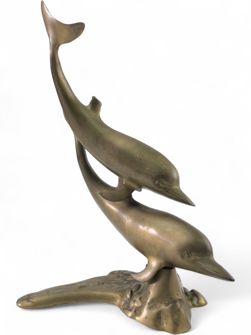 Brass Double Dolphin Sculpture, 15.5" tall: A sculptural depiction of two dolphins, crafted from brass. One dolphin is positioned above the other, both rising from a textured base. Features a warm, aged patina. Unsigned and unmarked. Measures 1