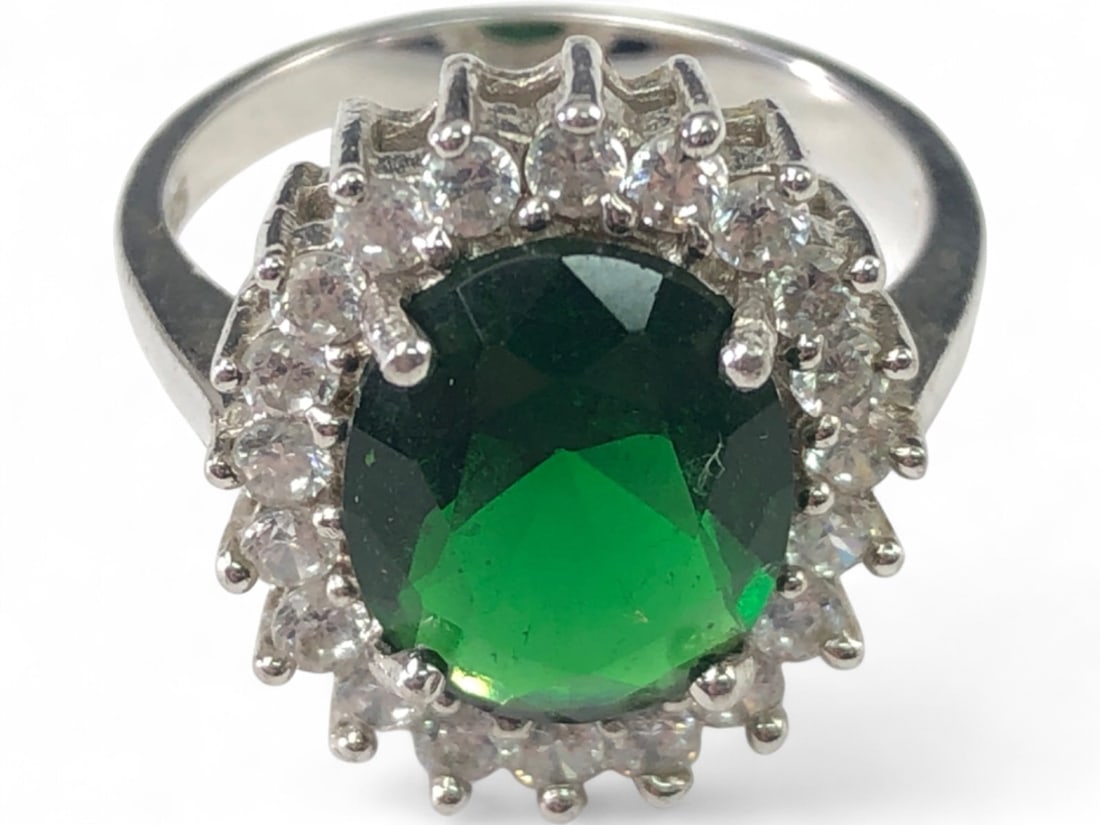 Sterling Green Crystal & CZ Cocktail Ring: Sterling silver cocktail ring featuring an oval-cut green crystal center stone surrounded by a halo of round-cut cubic zirconia (CZ) stones. The stones are prong-set in a cluster design. Marked '925' 