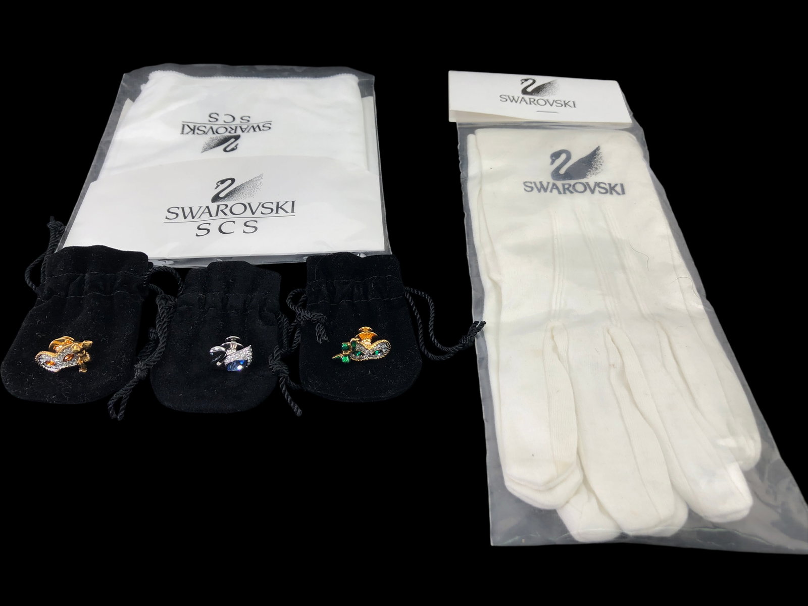 Swarovski SCS Crystal Pins, Gloves & Cleaning Cloth: Collection of Swarovski items including three crystal-embellished pins, a pair of white handling gloves, and a microfibre crystal cleaning cloth. Pins feature designs of a masquerade mask with clear a