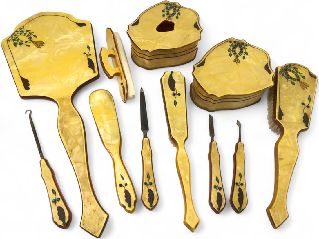 VTG Art Deco Celluloid Vanity Set 11pc Set: Art Deco period 11-piece vanity set crafted from pearlescent yellow and amber-toned celluloid. Features a stylized floral motif with green rhinestone accents and dark brown inlays. Set includes a hand