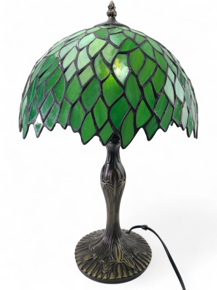 Tiffany Style Green Stained Glass Table Lamp: Tiffany style green stained glass table lamp, 18.5" tall. Features a domed shade with a leaf-like pattern in various shades of green, joined by dark solder lines. The ornate base is cast metal with an
