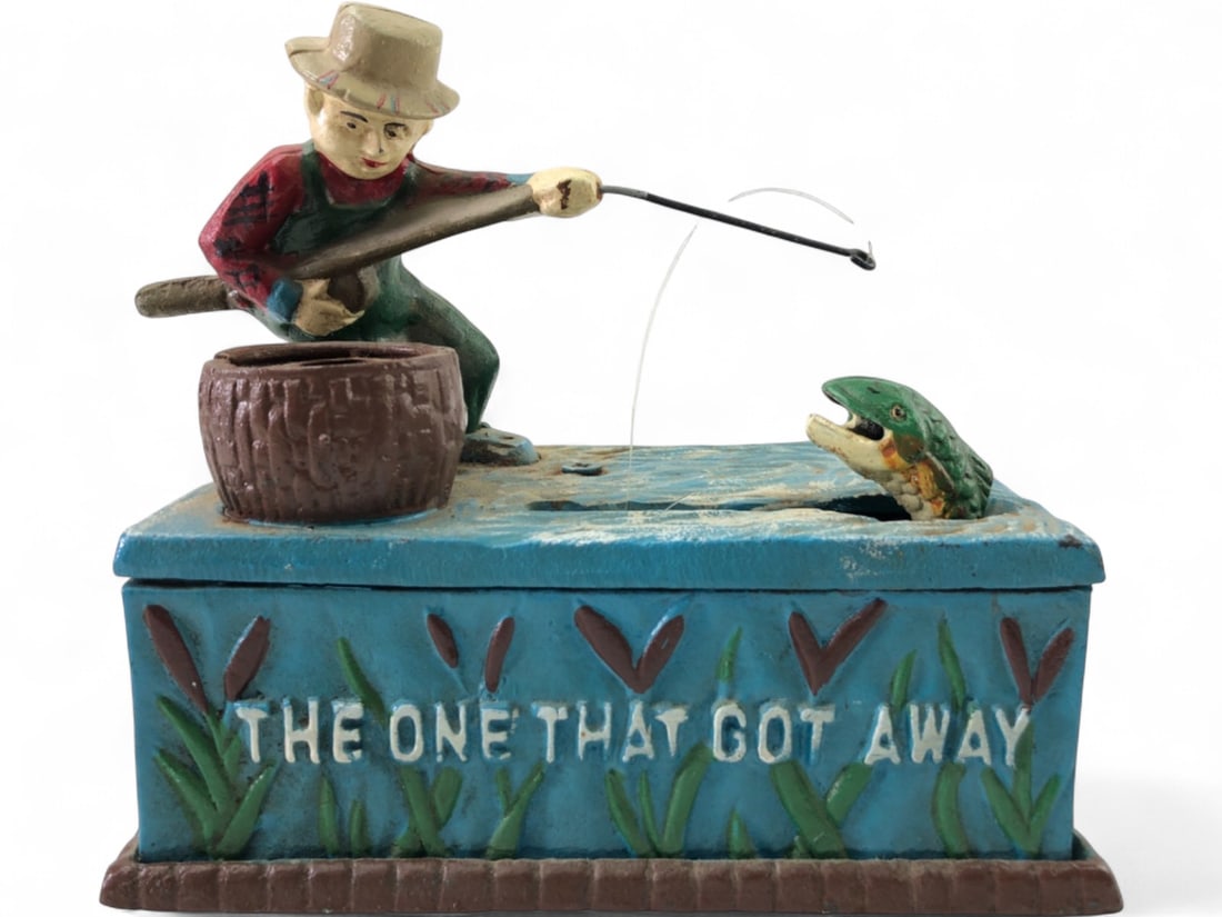 Cast Iron 'The One That Got Away' Bank: Antique cast iron mechanical coin bank, unmarked. Depicts a fisherman with a rod, a barrel, and a fish. When activated, a fish jumps to the barrel to deposit the coin. Front reads 'THE ONE THAT GOT AW