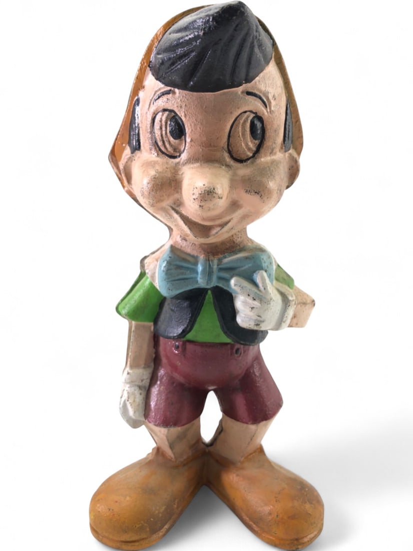 Cast Iron Pinocchio Coin Bank: Vintage cast iron Pinocchio coin bank, 9 3/4" tall. Depicts Pinocchio in his classic outfit. Two-piece construction with a coin slot on the back. Shows paint loss, surface wear, and minor rust consist