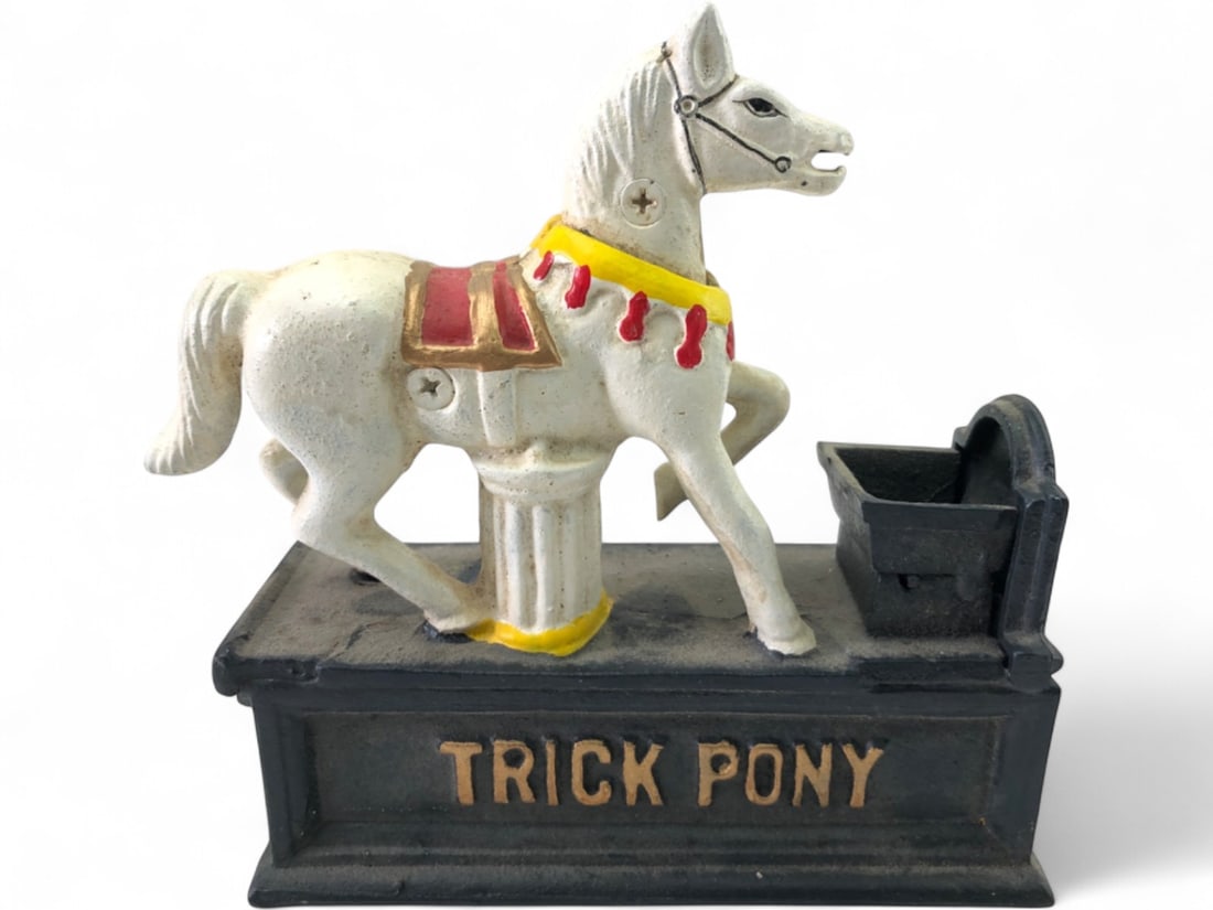 Cast Iron Trick Pony Mechanical Bank: Cast iron Trick Pony mechanical coin bank, a reproduction in the style of antique banks. Features a white pony with red and yellow accents on a black base, 'TRICK PONY' embossed on the front. A lever 